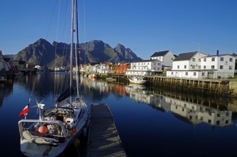 Sailing ships and wooden houses are reflected in the calm waters of a small harbour, Rorbuer,