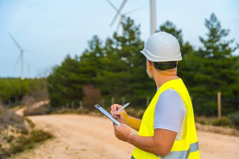 Rear view of a male mature engineer writing notes inspecting wind turbines in a green energy park