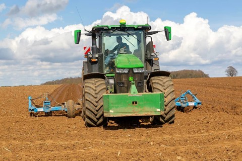 Green John Deere tractor ploughing deep furrows to prepare soil for potato crop, Ramsholt, Suffolk,