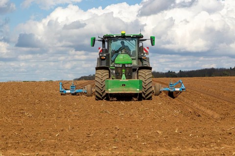 Green John Deere tractor ploughing deep furrows to prepare soil for potato crop, Ramsholt, Suffolk,