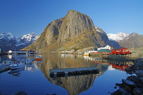 Barren mountains and red houses reflected in the calm waters of a fjord, winter, Hamnoey, Lofoten,