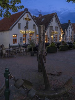 Ship's anchor on a wooden pile in front of restaurants at Greetsiel harbour at night, Greetsiel,
