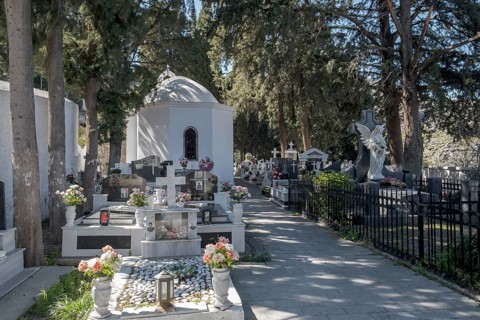 A white chapel surrounded by tombstones and an angel statue in a peaceful cemetery, Lindos, Rhodes,