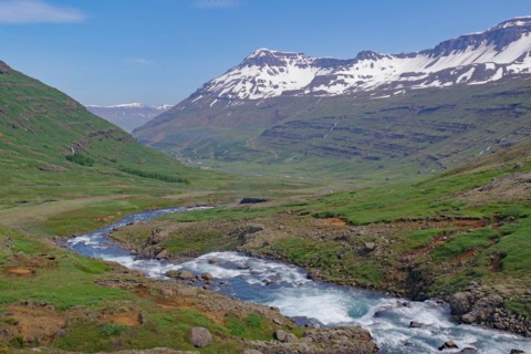 Water falls into a deeply incised valley framed by high mountains, ferry town, Seydisfjoerdur, East