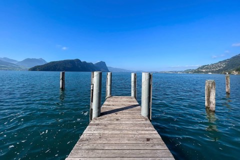 Wooden jetty juts into clear lake under blue sky, surrounded by mountains, Vitznau, Lucerne,