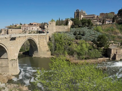 Stone bridge over the river, green hills with historical buildings and cathedral, clear blue sky,