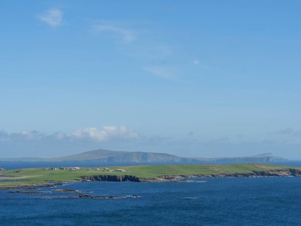 Vast coastal landscape with blue sky and green hills on the horizon, green meadows on a deep blue