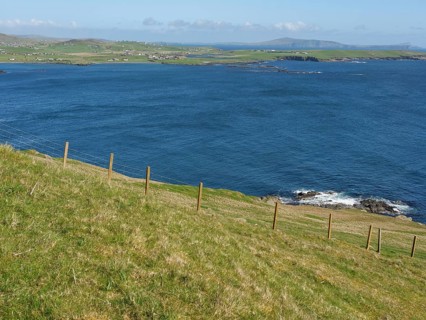 Green meadow leads to rocky coastline with sweeping views across deep blue sea, green meadows by a
