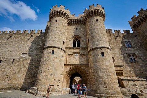 Super wide angle shot, travellers standing in front of an imposing crenellated old castle facade,