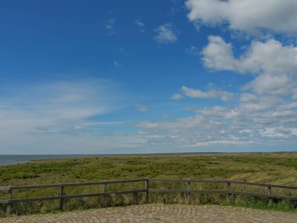 Extensive view of the sea and a green meadow under a partly cloudy sky, dune and beach by the sea