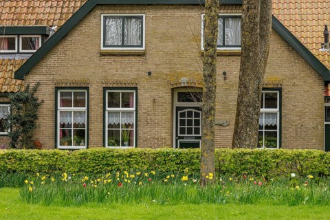 Front view of a cosy brick house with flower bed and green lawn, old houses with green gardens in a
