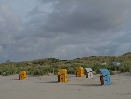 Beach chairs scattered on the beach under a cloudy sky, surrounded by gentle dunes, colourful beach