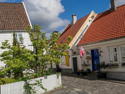 White houses with tiled roofs, lantern in front of plants and fence, cobblestone street under blue