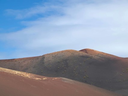 Dry, hilly desert area under a blue sky with white clouds, barren landscape of lava mountains,