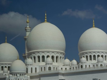 Detailed view of the white domes of a mosque with golden spires against a blue sky, large mosque