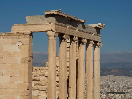 Ancient marble columns with a cityscape and mountains in the background under a clear sky,