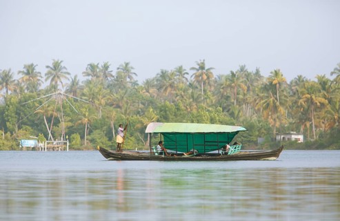 Indian man stakes his boat over the Cherai lagoon, behind blurred Chinese fishing net, Vypin