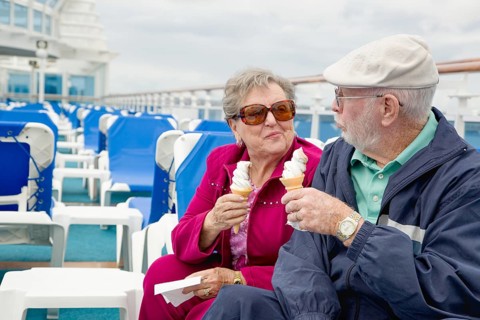 Happy senior adult couple enjoying ice cream on the deck of a luxury passenger cruise ship
