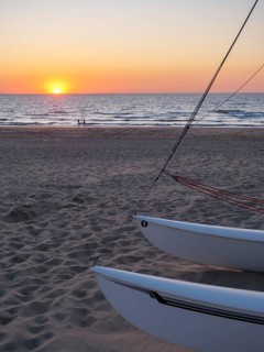 Boats on the beach at sunset, the sea glistens under the orange sky, a calm and relaxed atmosphere,