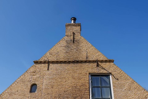 Brick house facade with chimney in front of a clear blue sky, minimalist look, historic houses in a