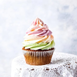 Cupcake with swirling pastel frosting on a matte grey backdrop, AI generated