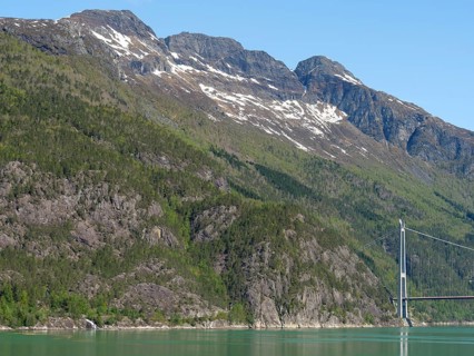 High mountains with remnants of snow on the peaks, green forested slopes and a large bridge under a