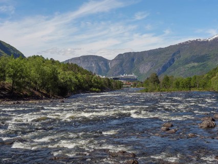 A river in a valley, surrounded by green forests and mountains, in the background a large ship,