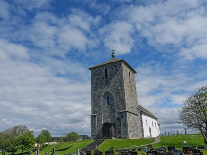 Historic church in a cemetery under a slightly cloudy sky, old stone church and many gravestones by