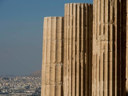 Close-up of ancient marble columns in front of a cityscape with clear sky, historical columns and