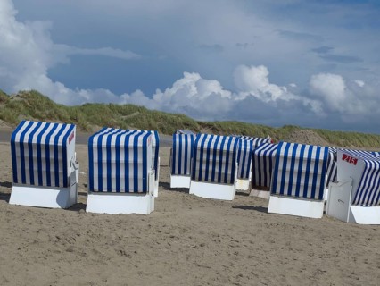 A group of blue and white beach chairs stands on the beach in front of grassy dunes and a cloudy