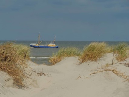 Sand dunes with a view of the sea and a boat under a cloudy sky, dune with dune grass and a boat by