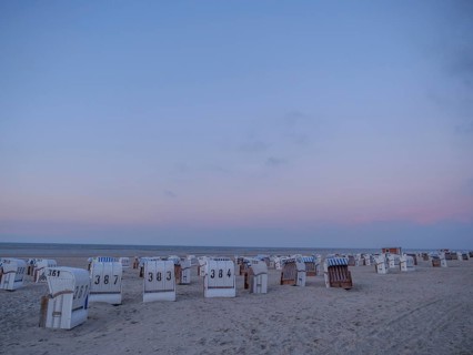 A quiet beach with white and striped beach chairs at dusk under a pastel-coloured sky, setting sun