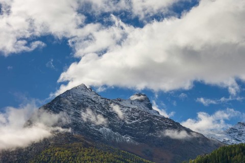 Snow covered mountain peak under a blue sky with scattered clouds, snow on high mountains in the
