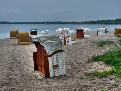 On the beach there are several beach chairs in different colours in front of a calm sea under a