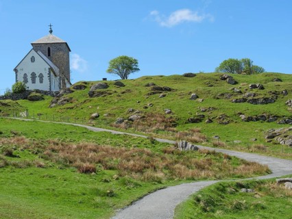 Church with hiking trail on hilly landscape, blue sky with clouds and trees, old stone church and