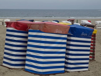 Several colourful beach chairs with stripe pattern standing on the beach in front of a cloudy sky,