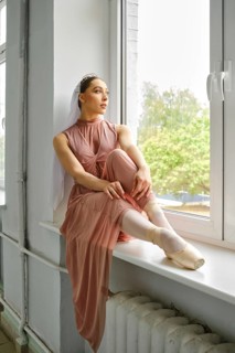 Ballerina sits thoughtfully on the windowsill and looks out the window during a break