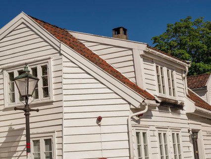 A white wooden house next to a street lamp and a green tree under a blue sky, white wooden houses