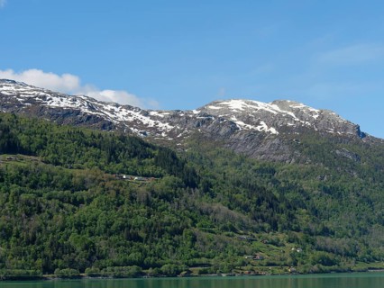 Green mountain slopes with snow-capped peaks, a lake and clear sky, greenish shimmering water in a