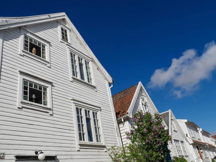 White wooden house with red tiled roof under clear blue sky, bright sun illuminates the facade and
