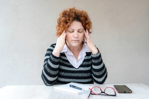 A mid-adult redhead woman with a headache is rubbing her temples