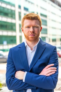 Vertical portrait of a confident young businessman looking at camera standing with arms crossed
