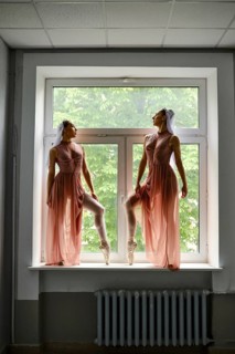 Two graceful ballerinas in transparent long dresses stand on the windowsill in the corridor