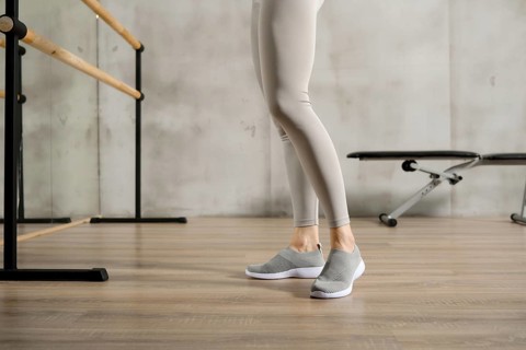 Slender female legs in sports leggings and sneakers near the handrail in the gym