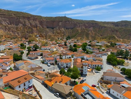 Panoramic view of a village with orange roofs, streets and green trees surrounded by mountains,