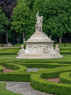 Monumental fountain with several sculptures in a well-kept baroque garden, park with green hedges,