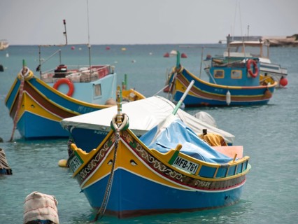 Several colourfully painted fishing boats anchor quietly in a harbour, surrounded by ropes and