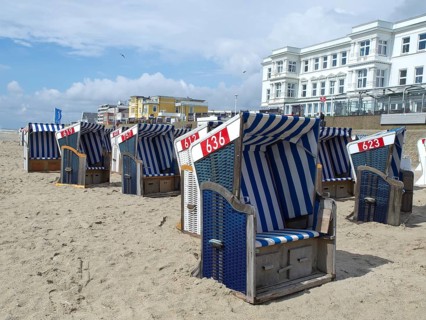 Blue and white beach chairs in a row on the beach in front of white buildings under a sunny sky,