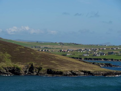 A small village on the coast with green fields and sea views, green meadows on a deep blue sea and