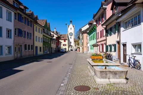 A picturesque old town street with colourful houses and a dominant clock tower under a clear blue